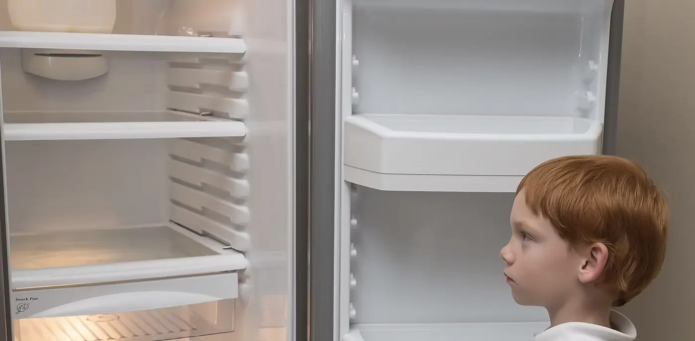 A young boy looking into an almost empty fridge