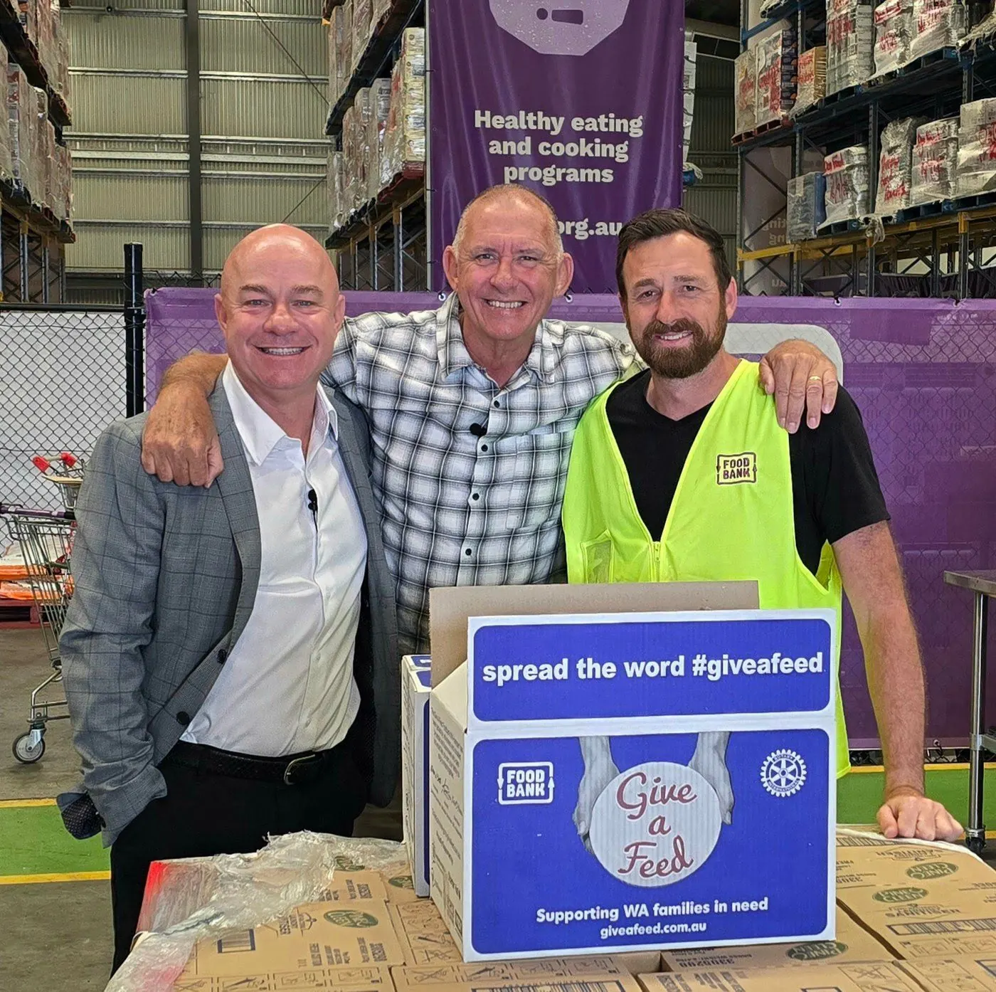 Aaron Pitt with supporters and a Foodbank WA volunteer behind a Give A Feed hamper box that reads spread the word #giveafeed